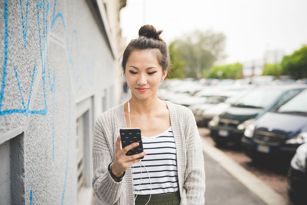 young beautiful asiatic woman holding a smart phone listening mu